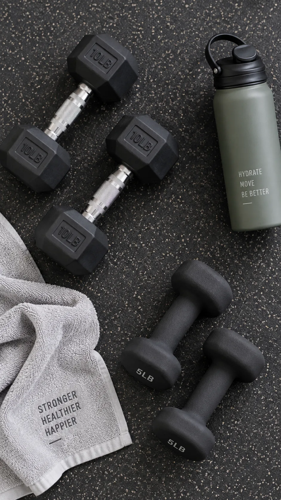 Flat lay of two sets of dumbbells on a gym floor with a workout towel and water bottle, clean minimalist fitness photography, overhead angle