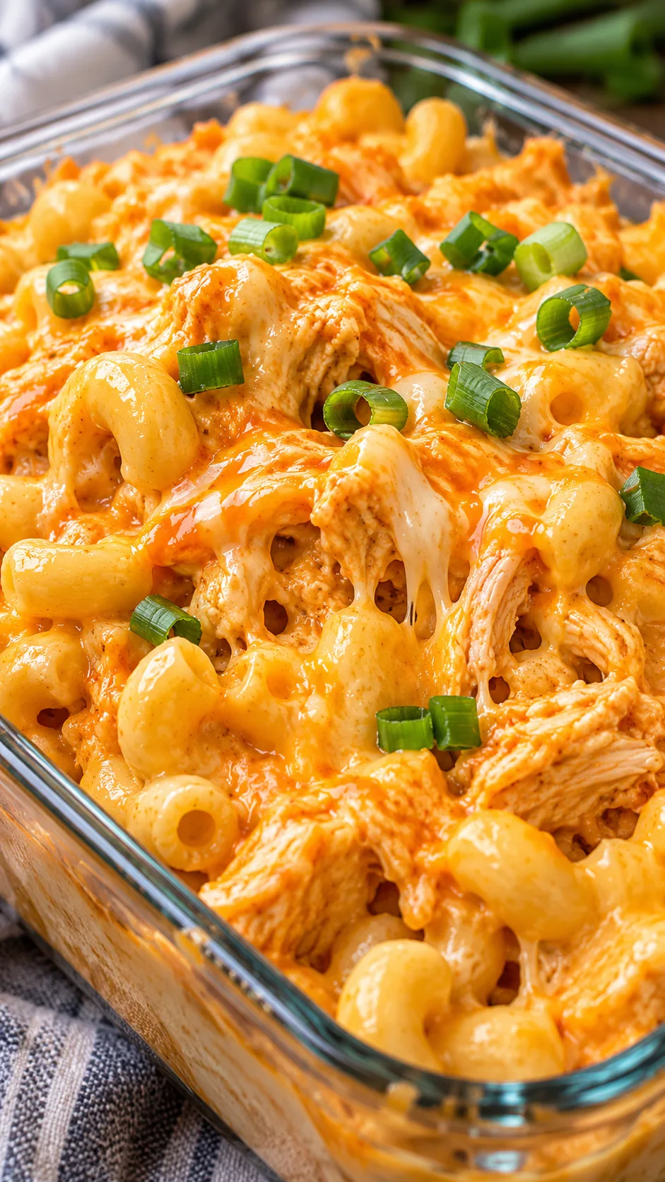Close up shot of creamy buffalo chicken mac and cheese garnished with green onions inside a glass container, showing melted high protein sauce texture