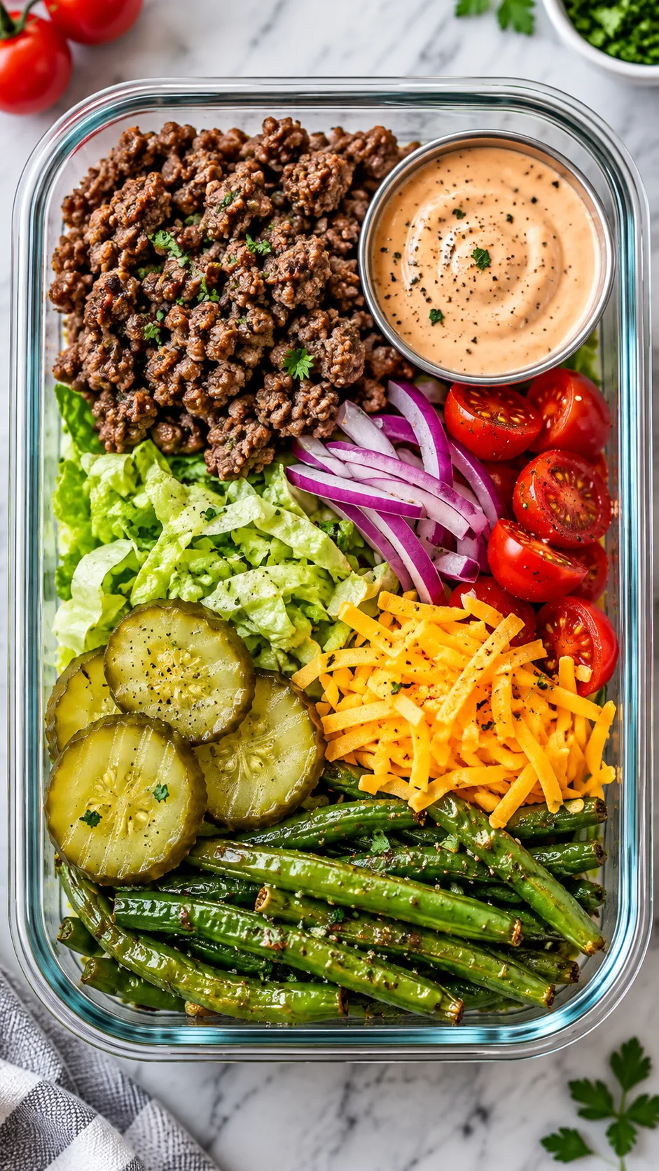 High-end realistic food photography of a low carb burger bowl meal prep container, seasoned lean beef, crisp lettuce, sliced pickles, cherry tomatoes, red onion, shredded cheddar, roasted green beans, creamy burger sauce in a small cup, overhead angle, vibrant natural colors