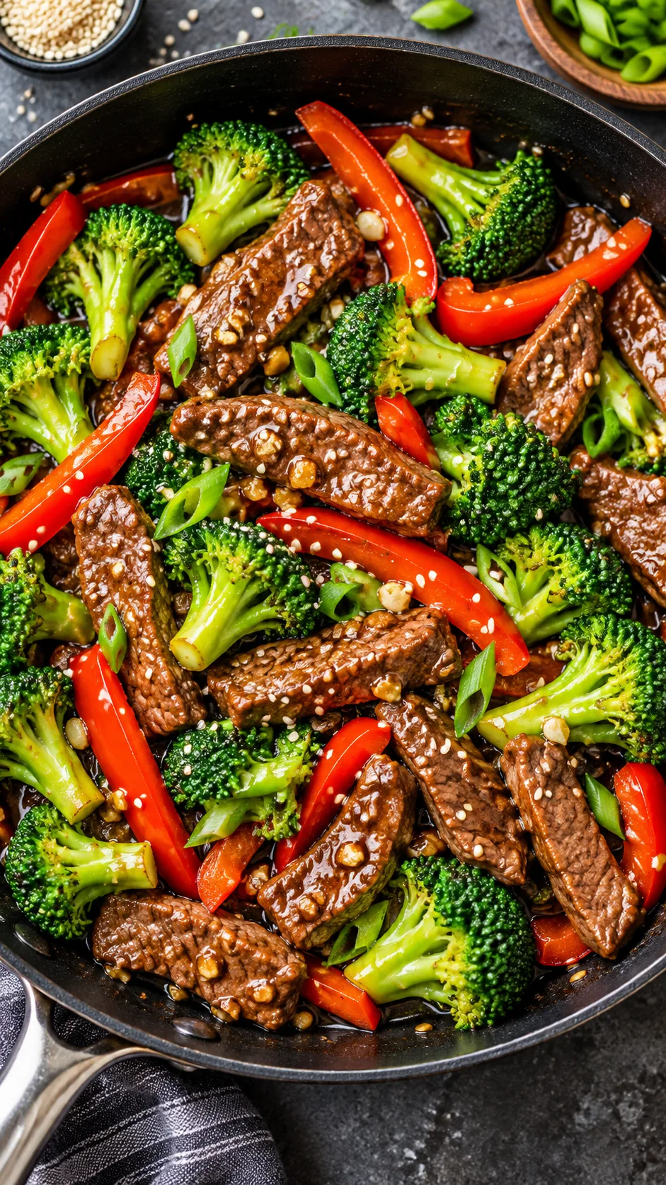 Overhead view of a vibrant beef stir fry with bright crisp broccoli florets, red bell pepper slices, and glazed sirloin strips in a black skillet